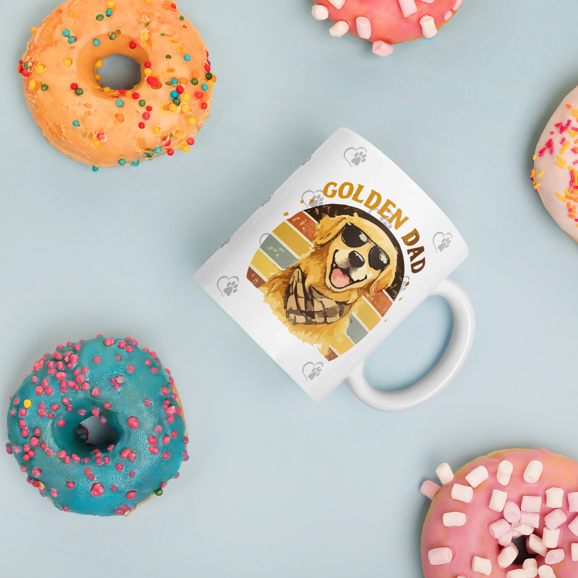 white-glossy-mug-white-11-oz-donuts-6a1b2b0708f25jpg - Golden Retriever Gift Shop Optional tagline if the builder asks for one: Life is Better with Goldens Donuts with pink and blue icing and colorful sprinkles on a pale blue background, with a partial mug and dog-themed magazine nearby.
